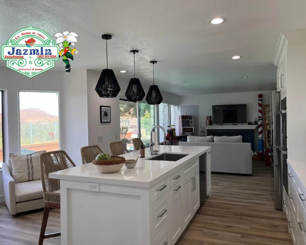 Bright modern kitchen with a white island, black pendant lights, and a view into a cozy living room.