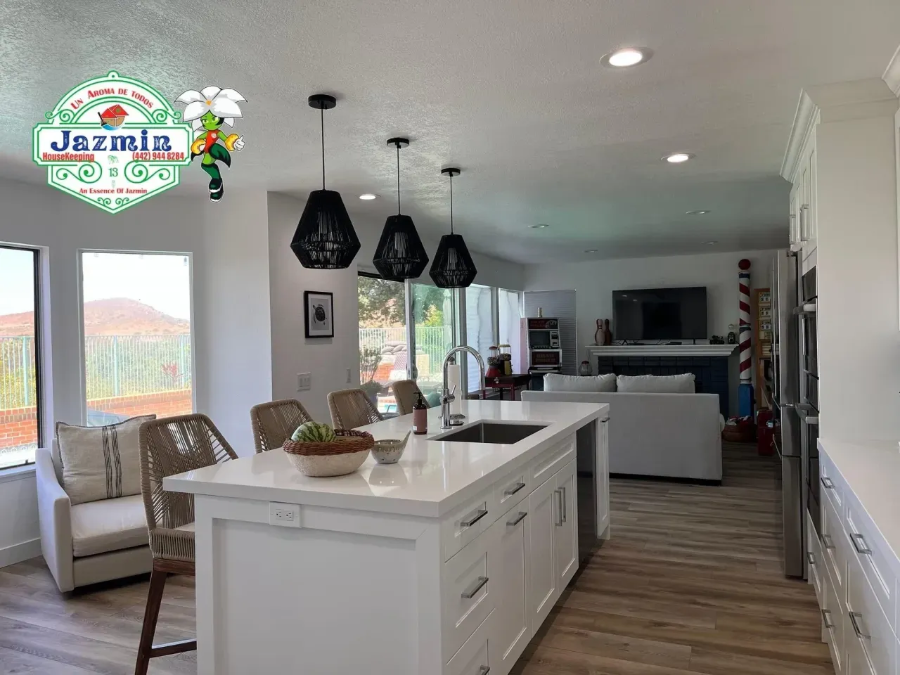 Bright modern kitchen with white island, black pendant lights, and open living area with large windows.