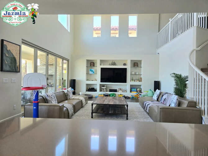 Bright, modern living room with tall windows, white walls, gray sofas, and a TV wall.
