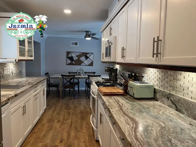 Modern kitchen with white cabinets, wood floors, marble countertops, and a dining area in the background