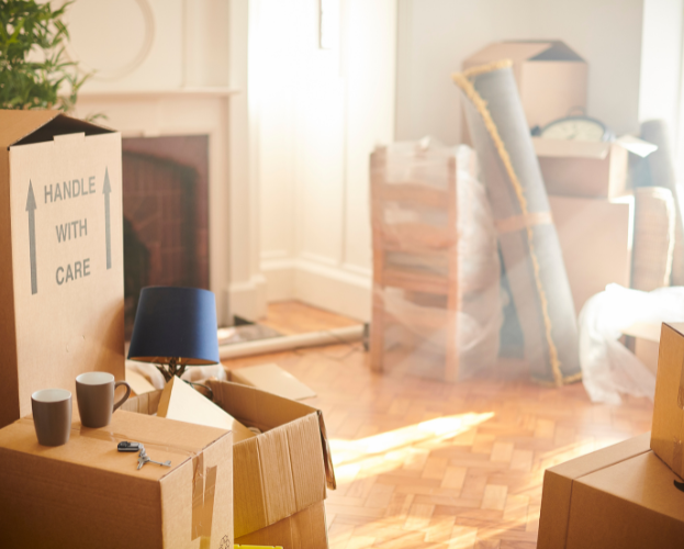 Cardboard boxes and packed furniture in a sunlit room, suggesting moving or storage.