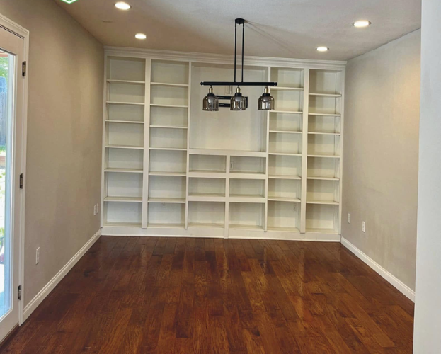 Empty dining room with white built-in shelving, hardwood floor, and a pendant light over the center.