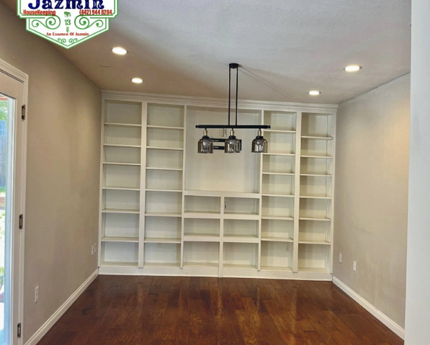 Empty room with white built-in shelves, hardwood floor, beige walls, and recessed ceiling lights