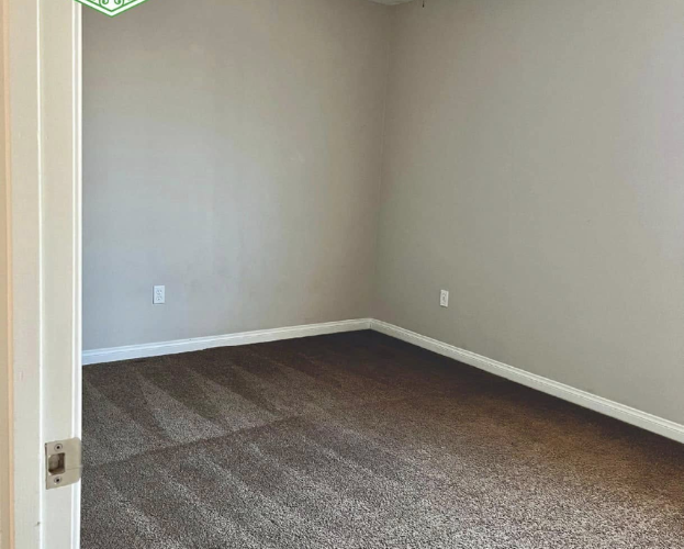 Empty carpeted room with gray walls and white trim, viewed through an open door