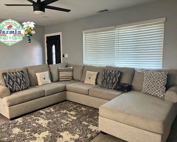Modern living room with gray sectional sofa, patterned pillows, rug, ceiling fan, and large window blinds