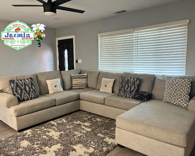 Modern living room with gray sectional sofa, patterned rug, ceiling fan, and white blinds.