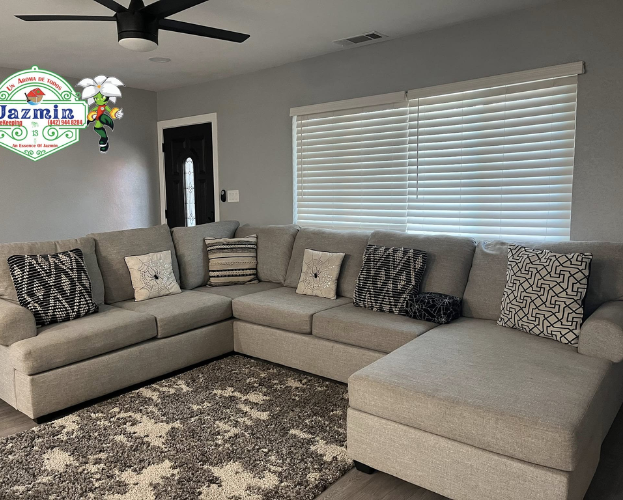 Gray sectional sofa with patterned pillows in a bright living room, under a ceiling fan and window blinds.