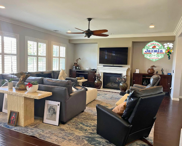 Bright living room with gray sofas, black chairs, wood tables, fireplace, TV, and ceiling fan