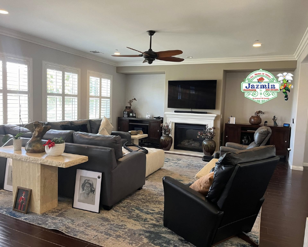 Bright living room with gray sofas, black chair, fireplace, TV, and large windows with shutters
