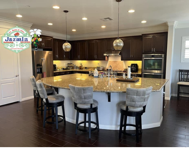 Modern kitchen with a large granite island, four stools, dark cabinets, and stainless steel appliances