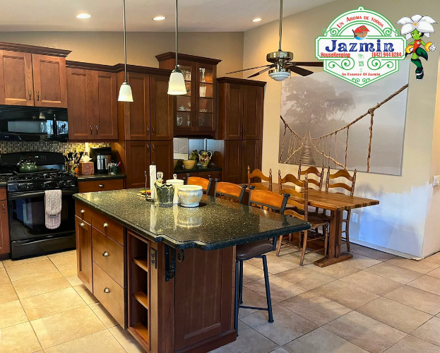 Modern kitchen with dark wood cabinets, granite island, tile floor, and dining table by a sunlit window