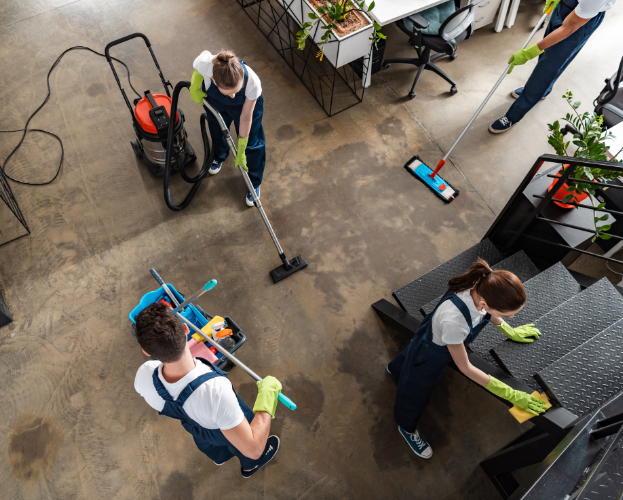 People cleaning a large indoor floor with mops and vacuum equipment near potted plants