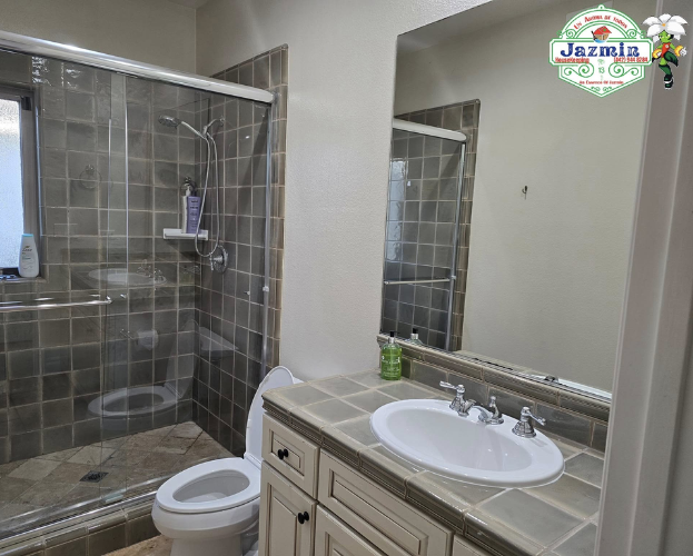 Bathroom with glass shower, toilet, and vanity sink with mirror and beige tile floor