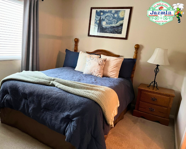 Cozy bedroom with a neatly made bed, blue bedding, nightstands, lamp, and framed wall art