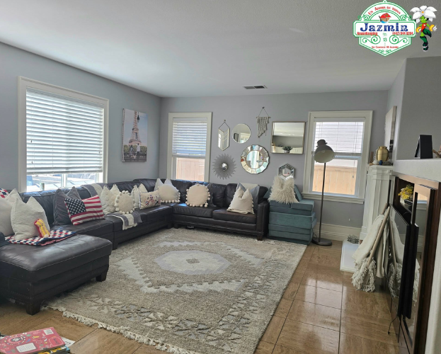 Bright living room with dark sectional sofa, patterned rug, wall mirrors, and a fireplace