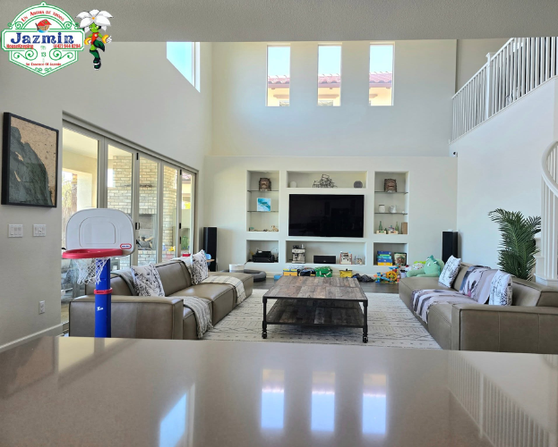 Bright modern living room with sofas, TV wall, tall windows, and a reflective floor