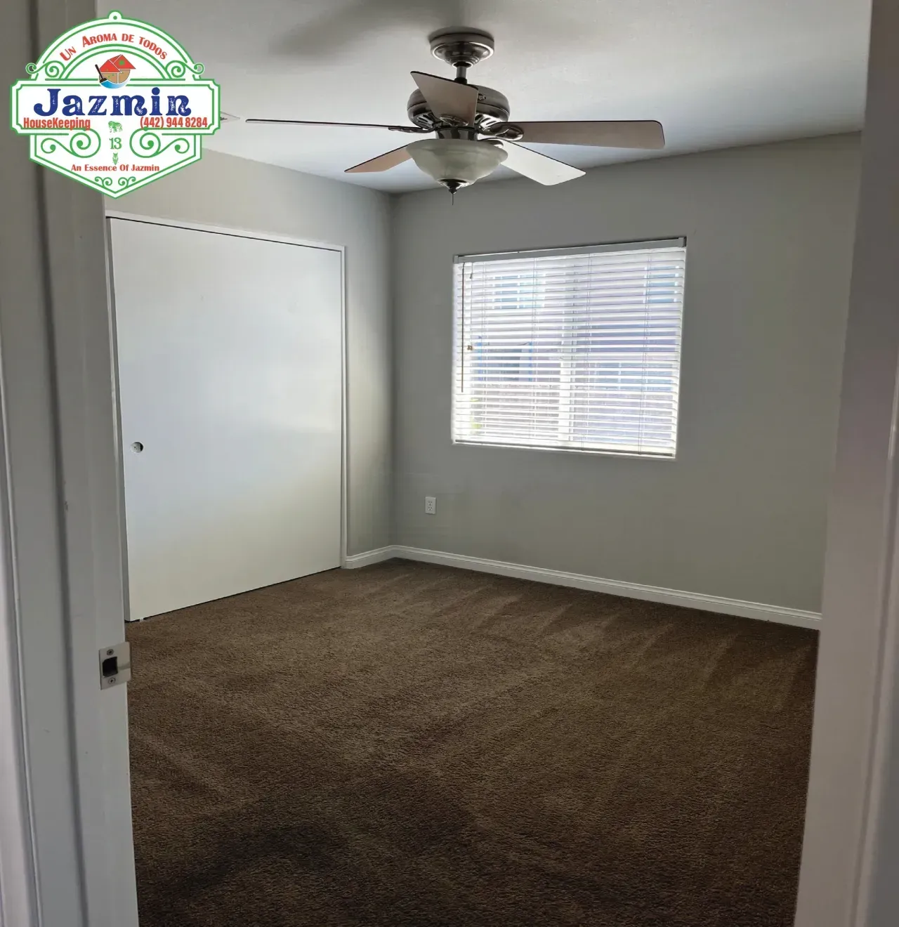 Empty carpeted bedroom with gray walls, white closet doors, window blinds, and a ceiling fan.