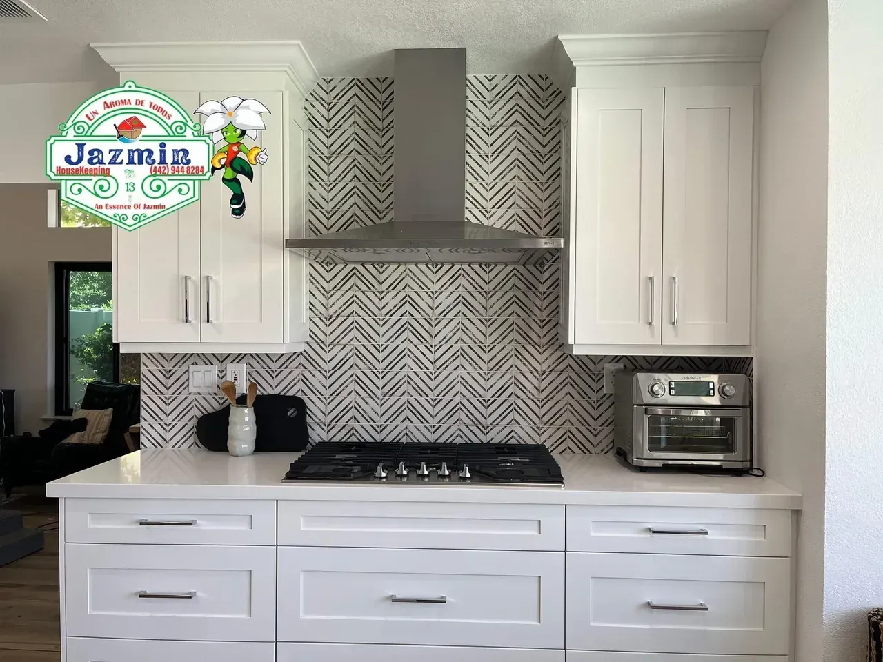 White kitchen with chevron backsplash, stainless range hood, and white cabinets and island.