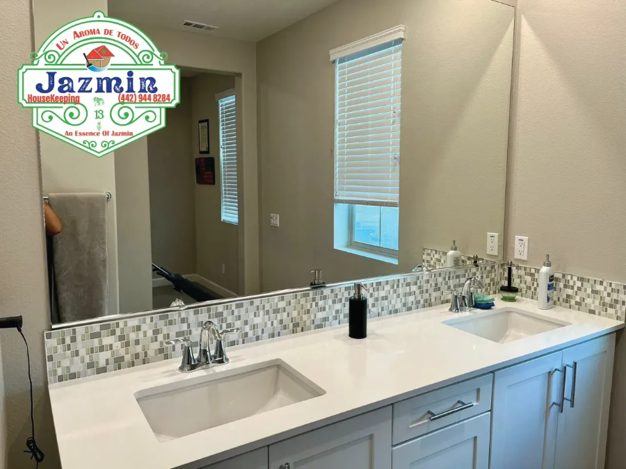 Bright bathroom vanity with double sinks, large mirror, blue cabinets, and window blinds