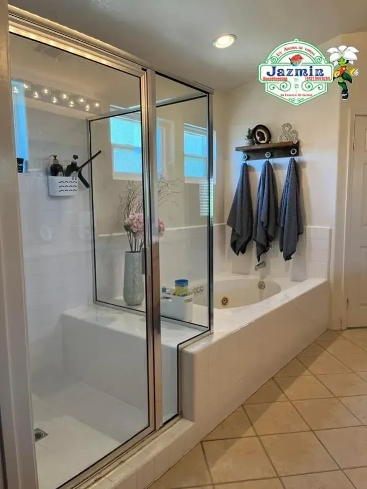 Modern bathroom with glass shower, white tub, towel hooks, and beige tile floor.