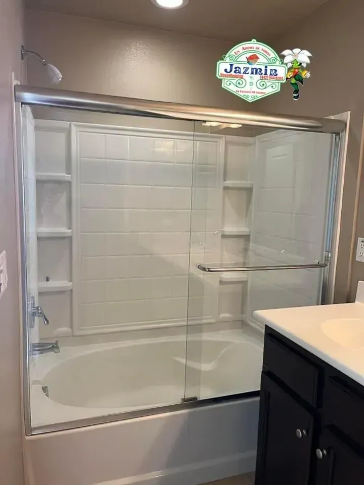 Empty tiled bathroom shower with glass sliding doors, built-in shelves, and a corner vanity in front.
