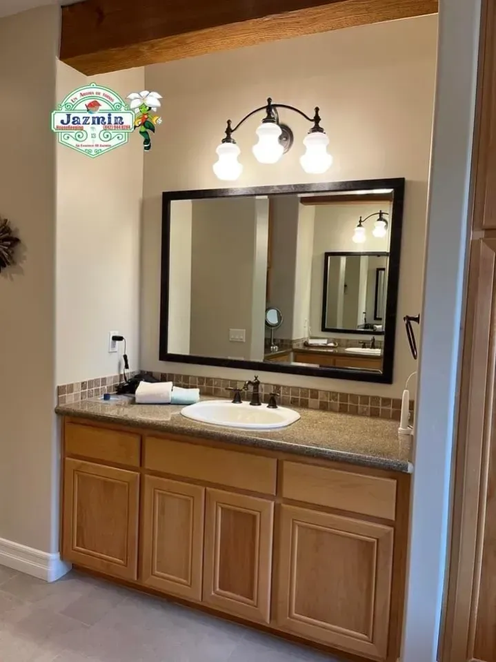 Bathroom vanity with double sinks, large mirror, wood cabinets, and wall light fixture