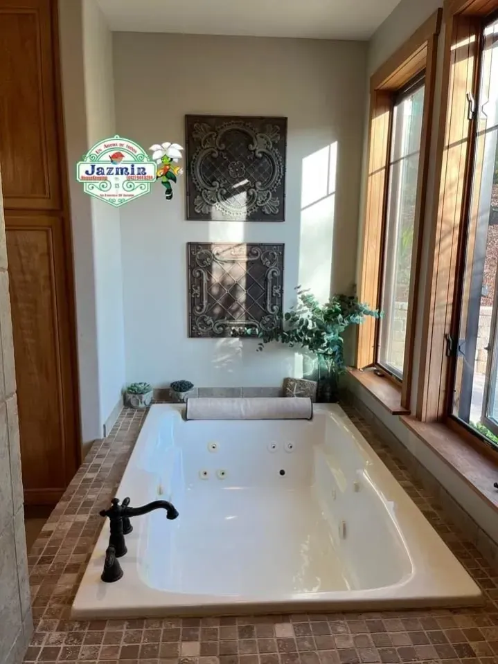 Bright bathroom with a white freestanding bathtub, black faucet, and large windows letting in sunlight.