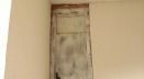 A wooden door is sitting on a white wall next to a window.