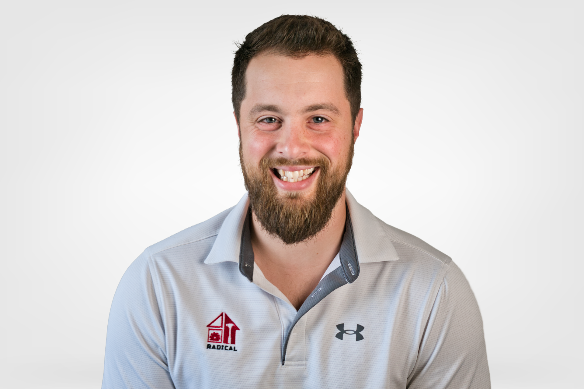 Smiling man in a light gray polo shirt with logos against a white background