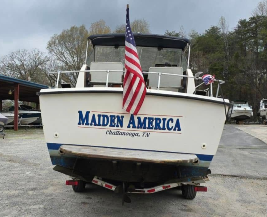 Boat named “Murder America” with an American flag, parked in a marina lot