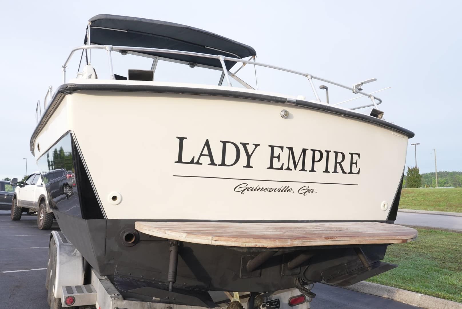 White boat named Lady Empire on a trailer, viewed from the stern near the water.