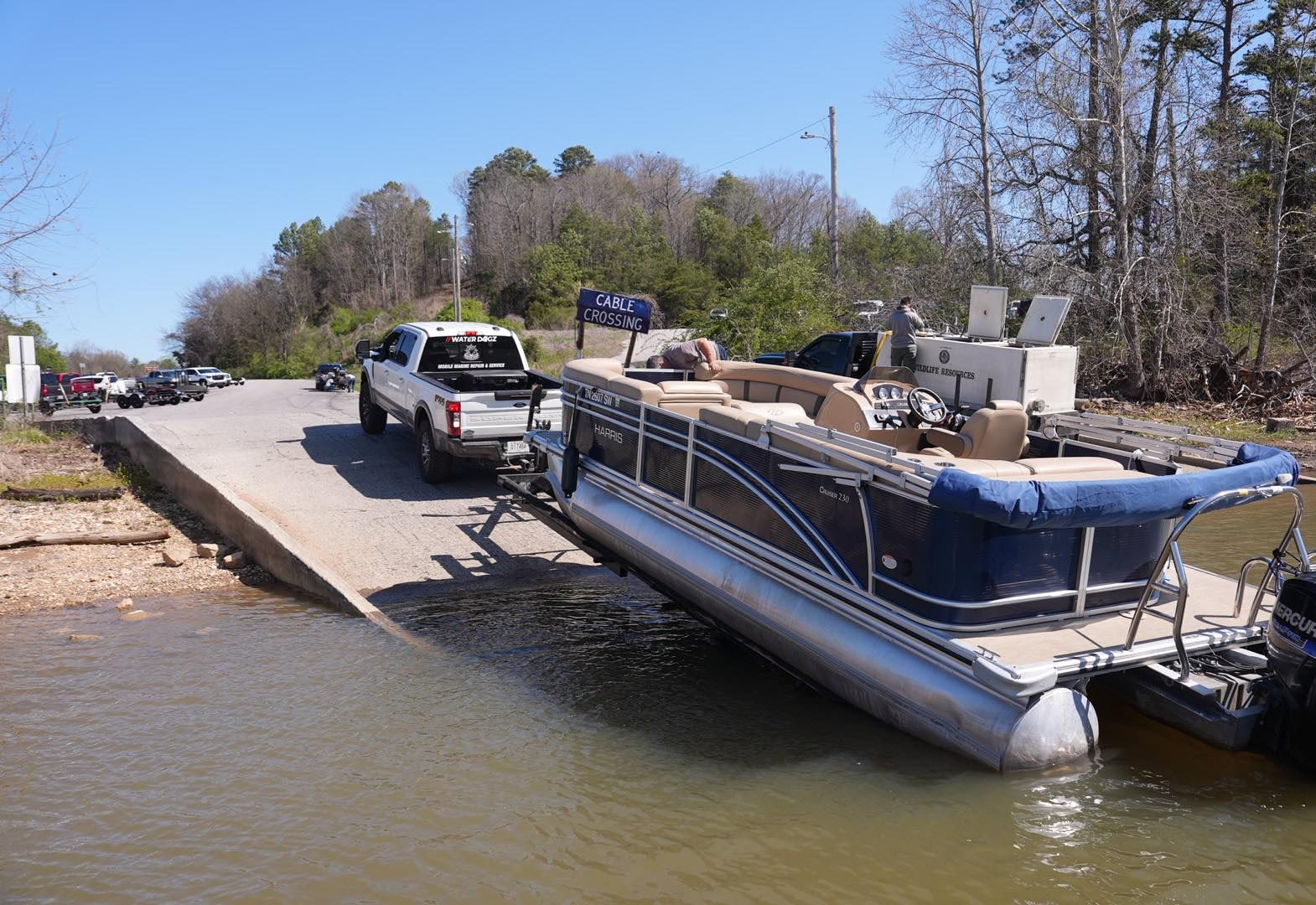 Pontoon boat and pickup truck on a low dock ramp at the water’s edge