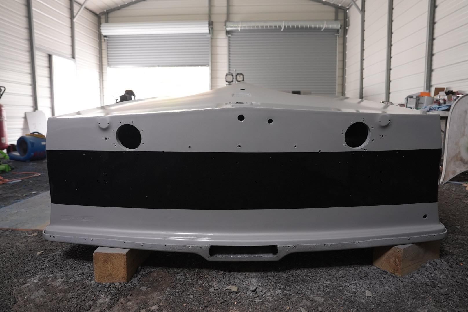 Front view of a white boat hull with a black stripe, sitting on blocks in a workshop.