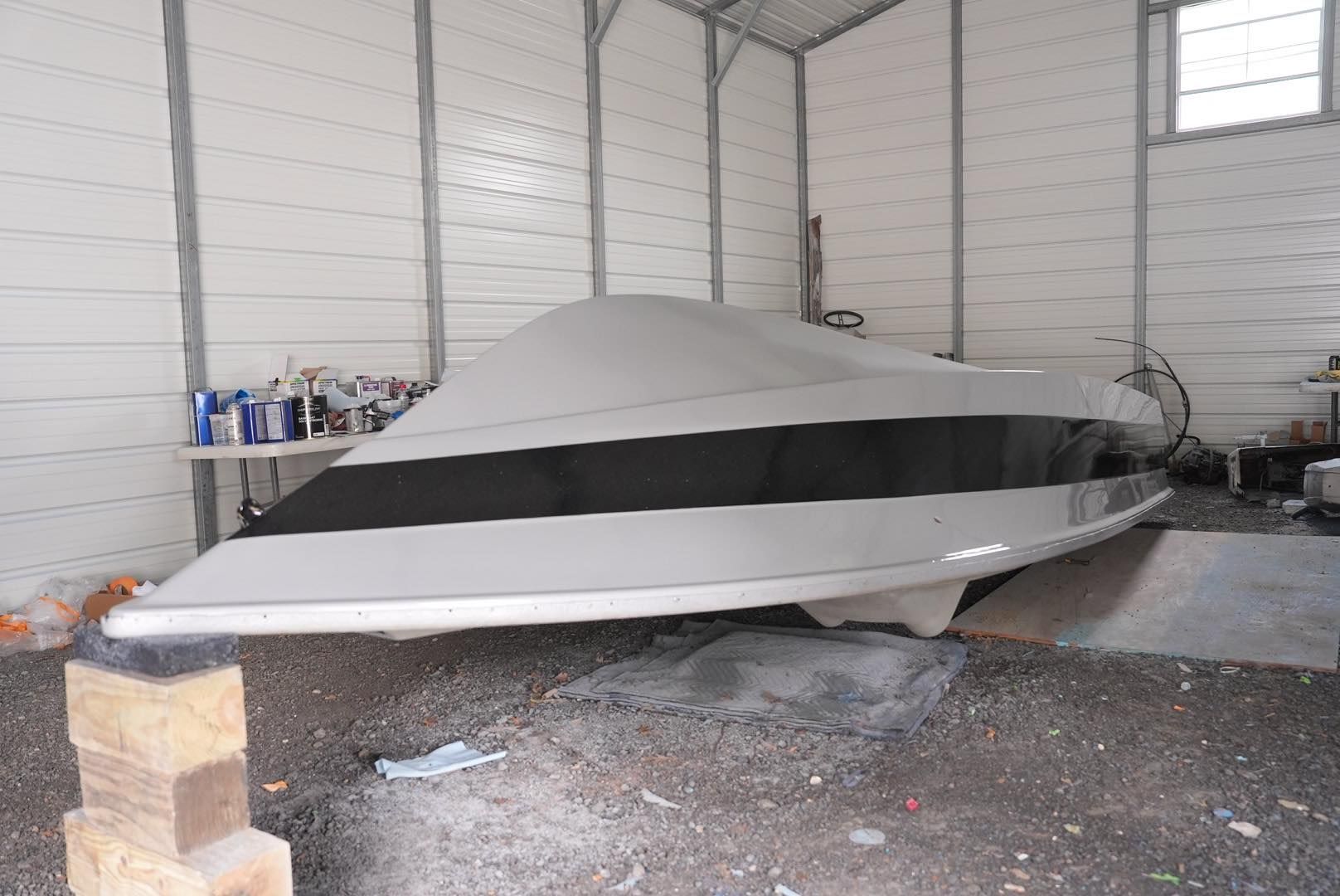Covered white boat stored indoors in a shed, with a black stripe along the side.
