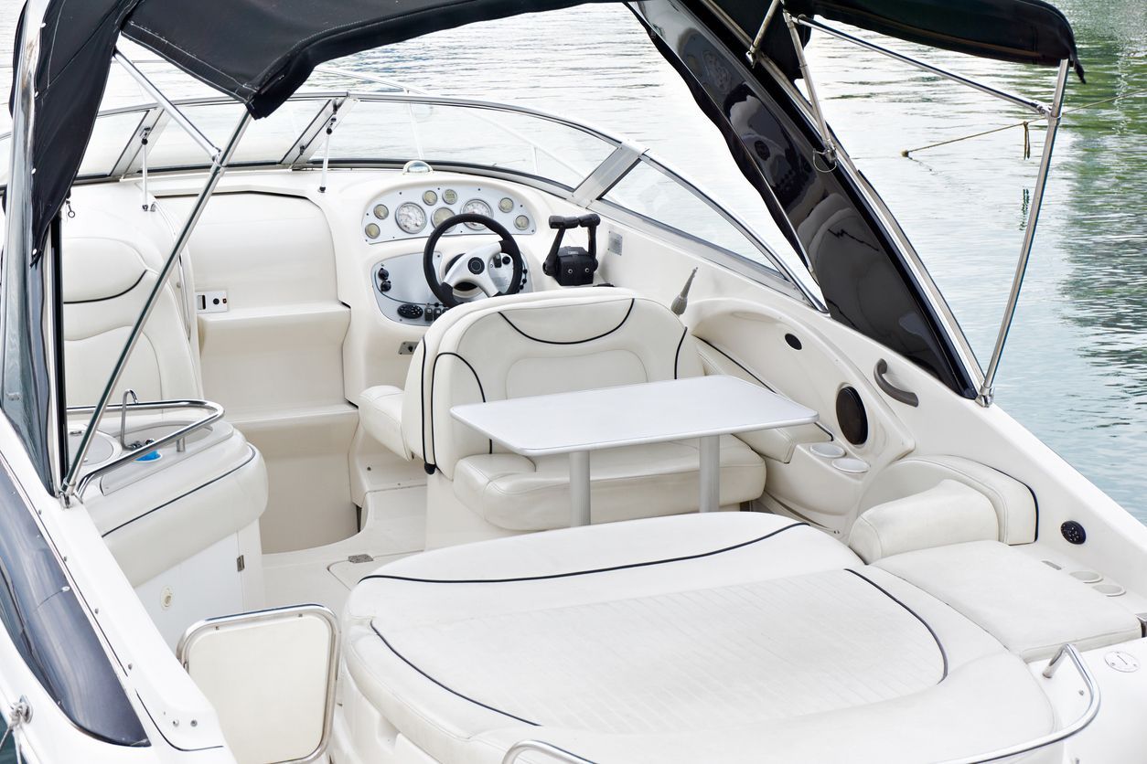 White boat cockpit with cushioned seats, steering wheel, and windshield on the water