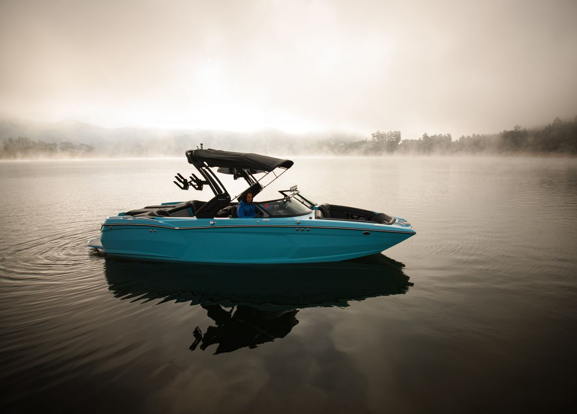 Turquoise speedboat on calm misty water at sunrise, with a wakeboard tower and soft reflections