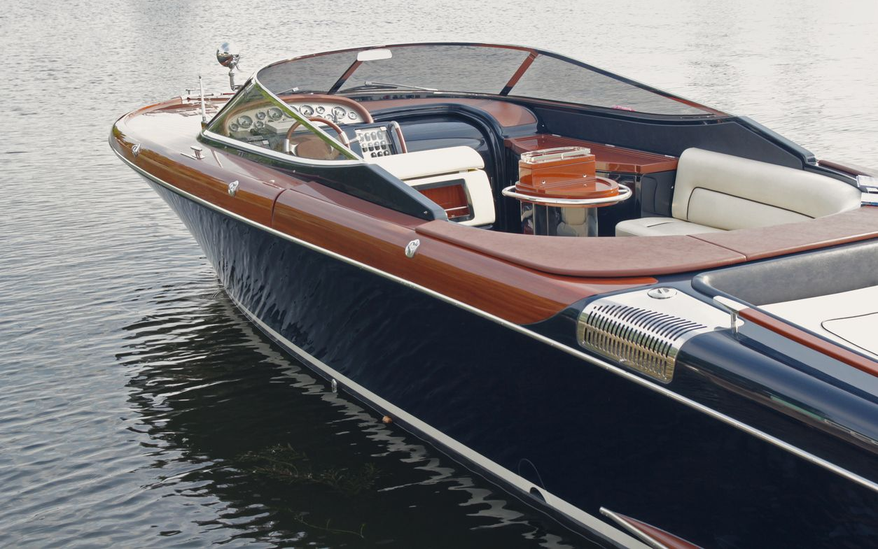 Luxury navy-and-wood motorboat gliding on calm water, with beige seating and a sleek windshield.