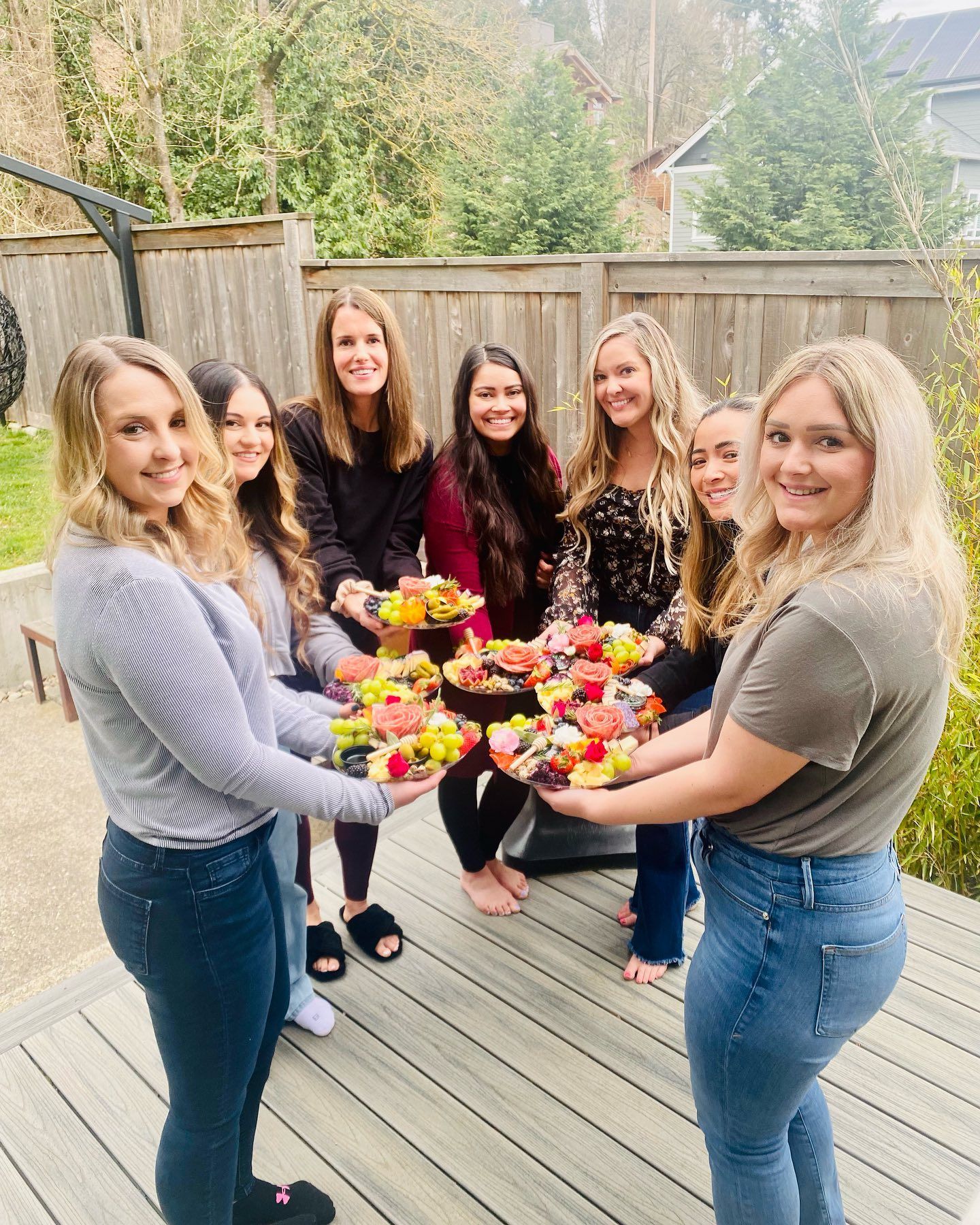 Group of women holding platters of fruit outdoors on a deck.