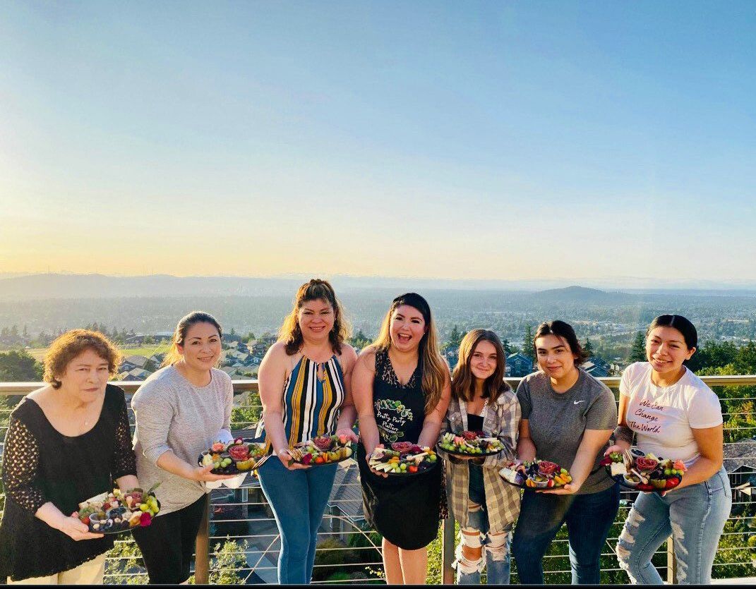 Seven people holding fruit bowls outdoors with a scenic view, sunset.
