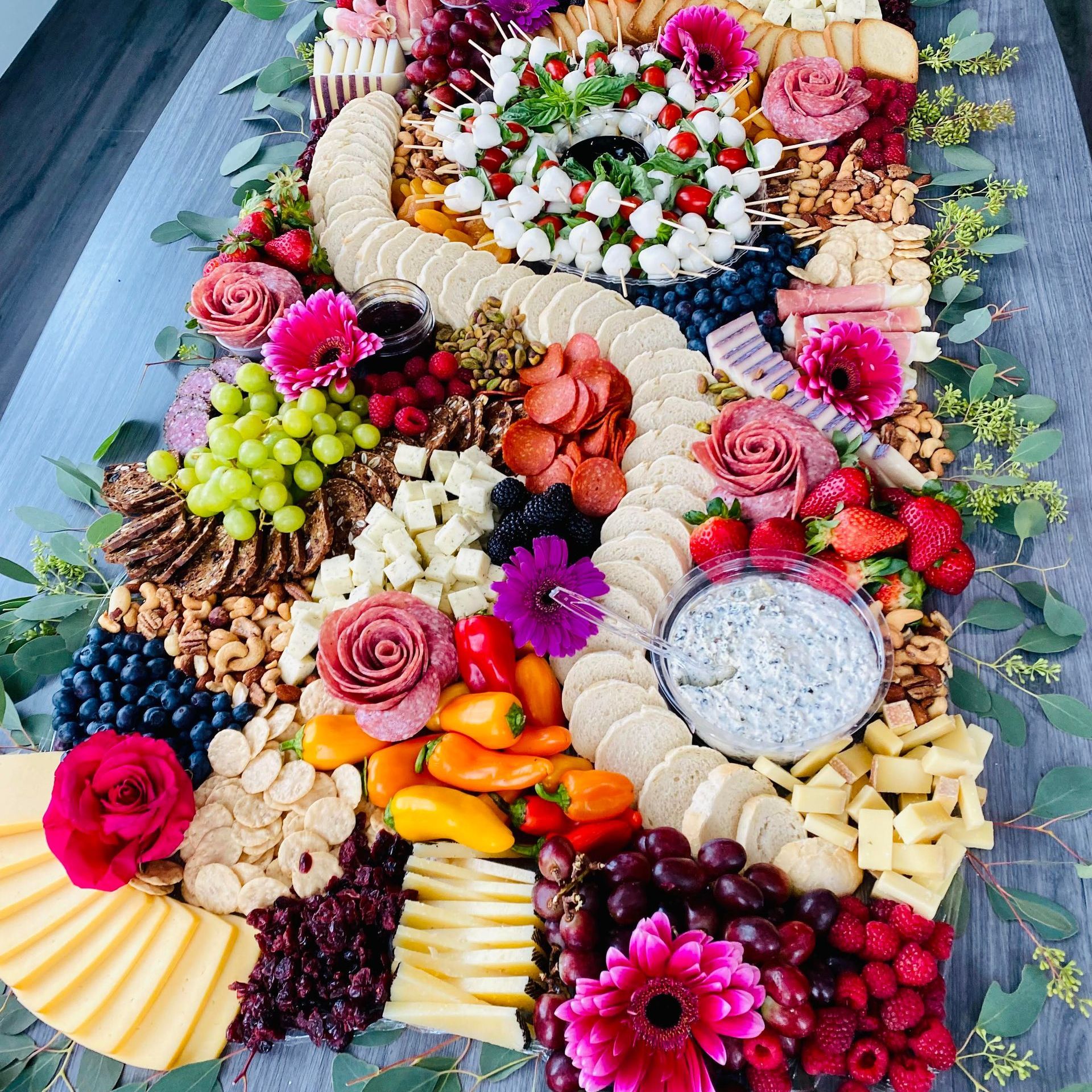 Charcuterie board with cheese, crackers, fruit, and flowers.