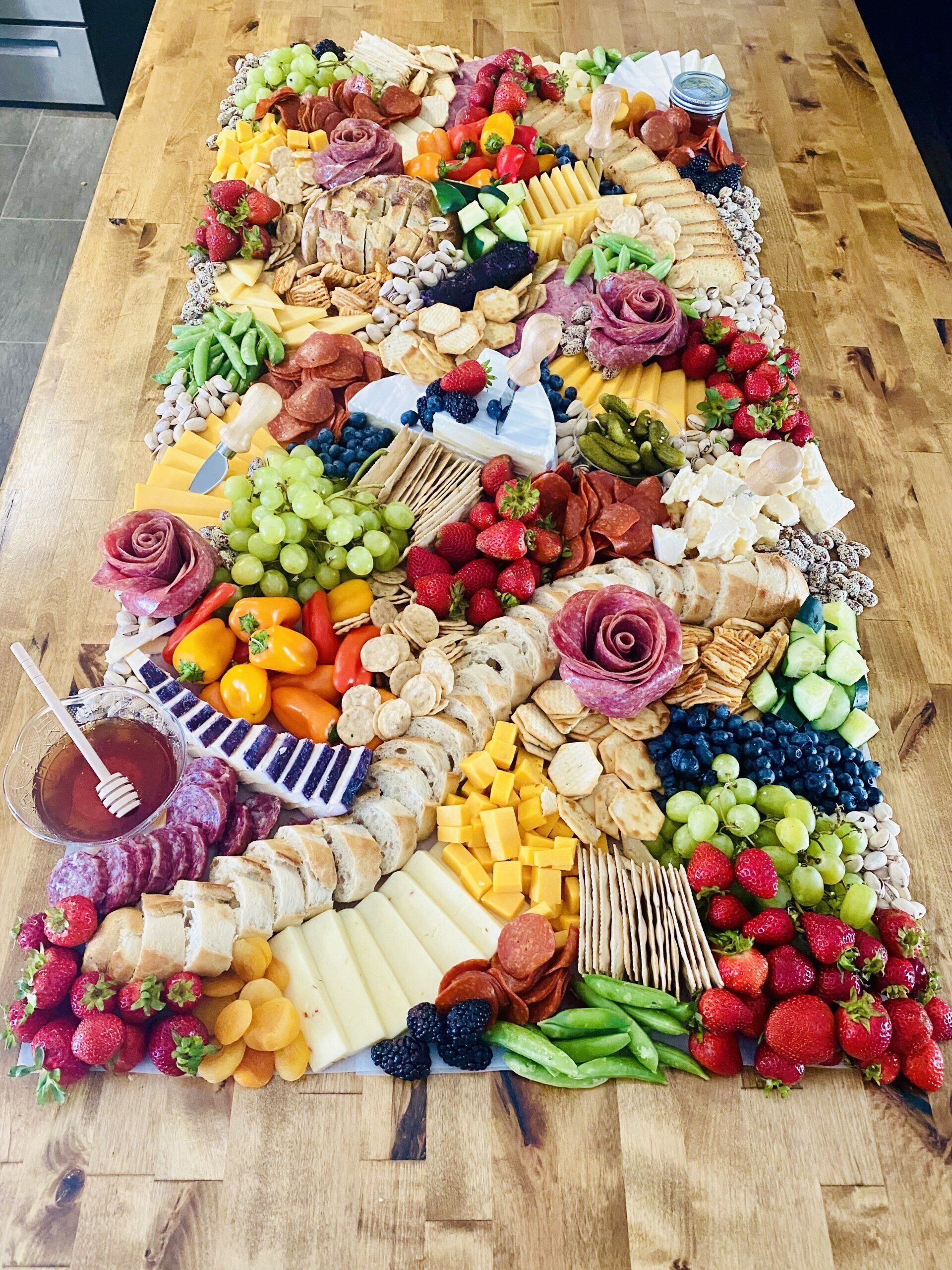 Large, rectangular charcuterie board on a wooden table, overflowing with fruits, cheeses, crackers, and meats.