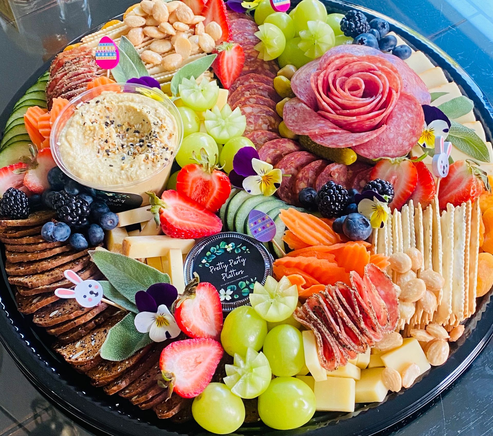 Charcuterie board with hummus, cheese, fruit, salami rose, and crackers.