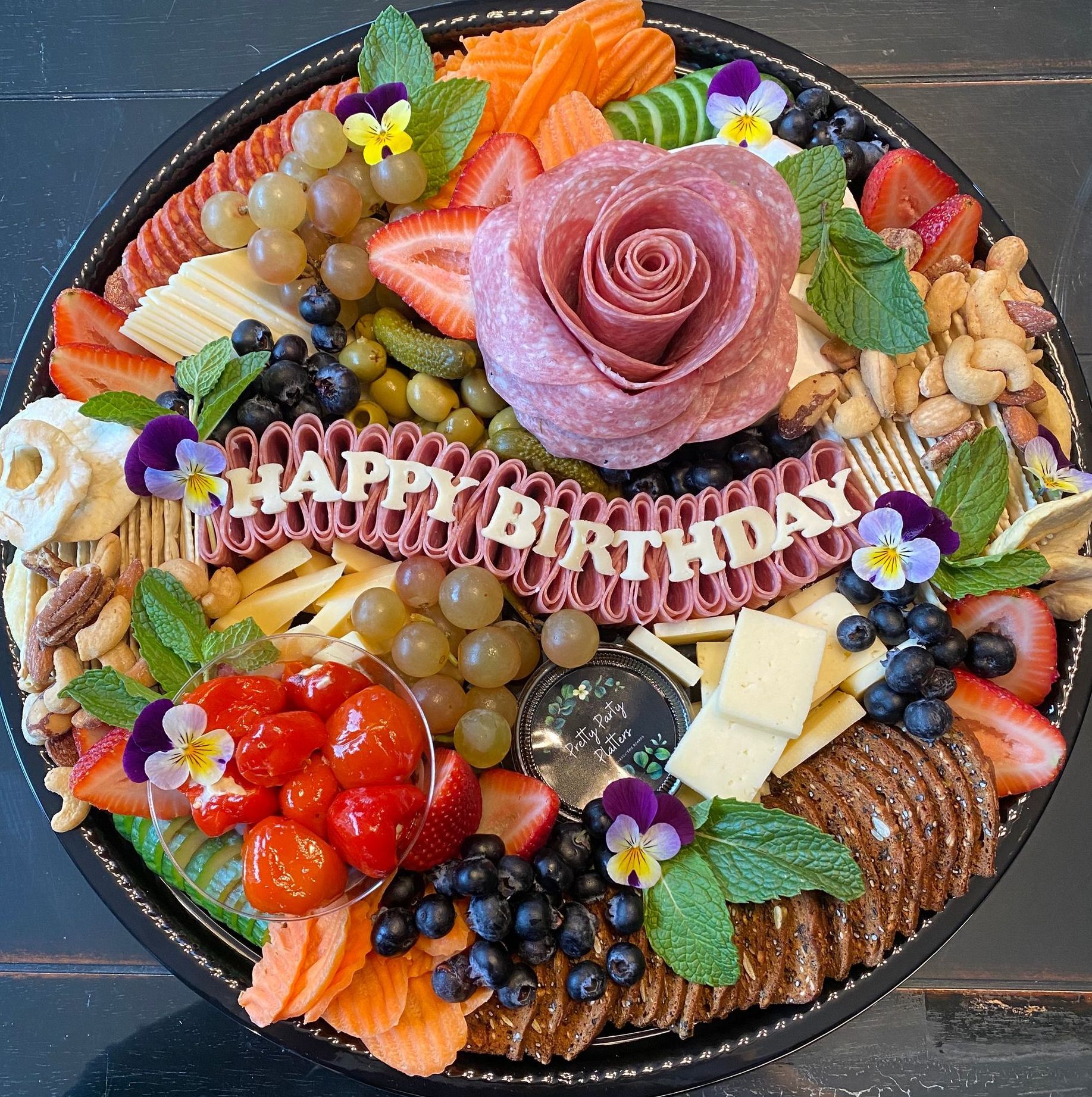Charcuterie board with salami rose, fruit, cheese, crackers, nuts, and