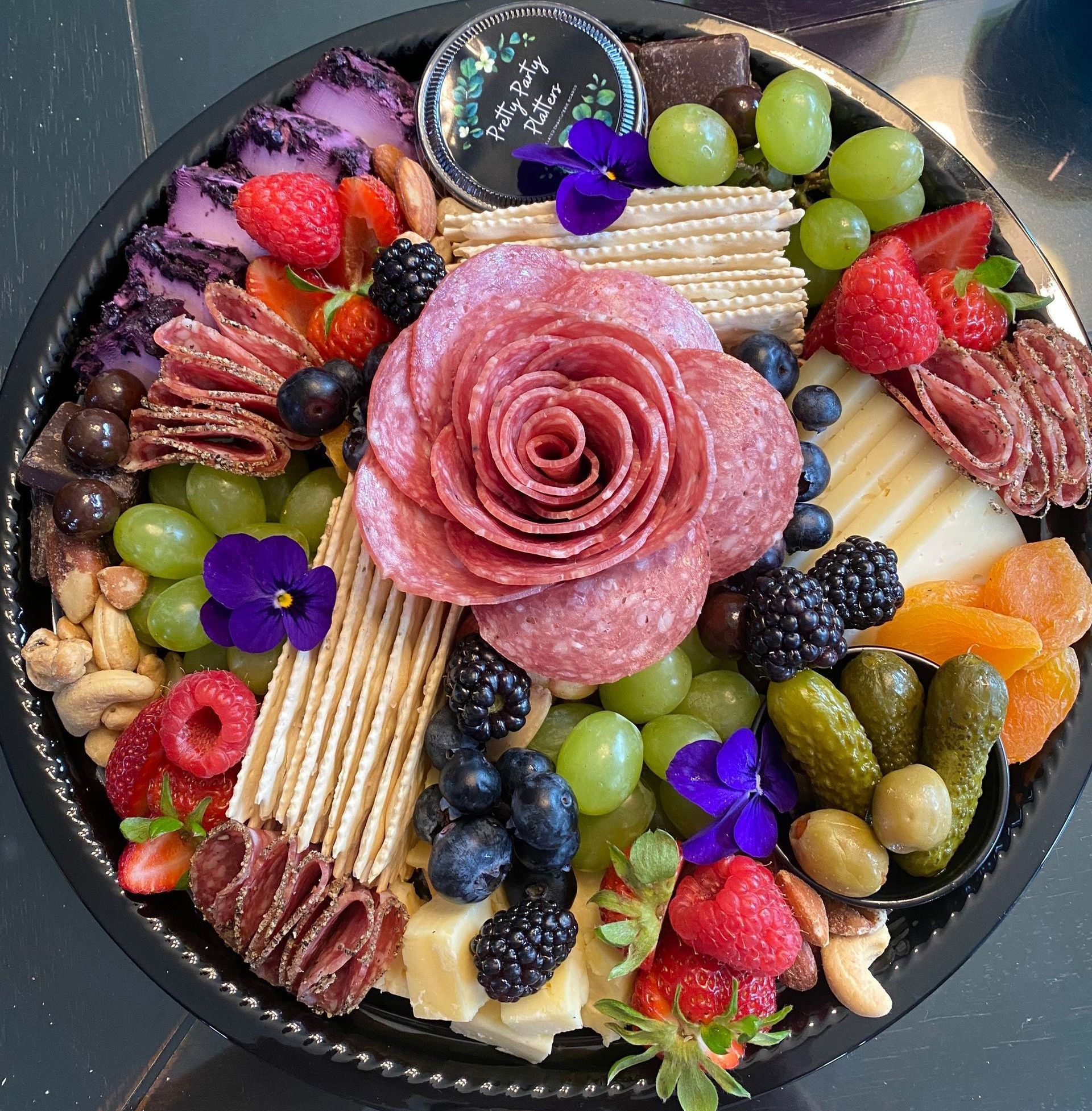 Charcuterie platter: Salami rose, cheese, crackers, fruit (berries, grapes), nuts, pickles, edible flowers.