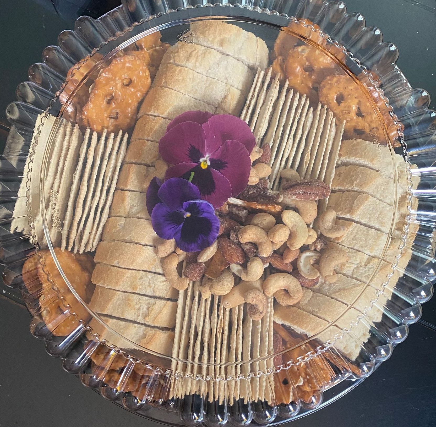 Charcuterie tray with bread, crackers, nuts, pretzels, and flowers.