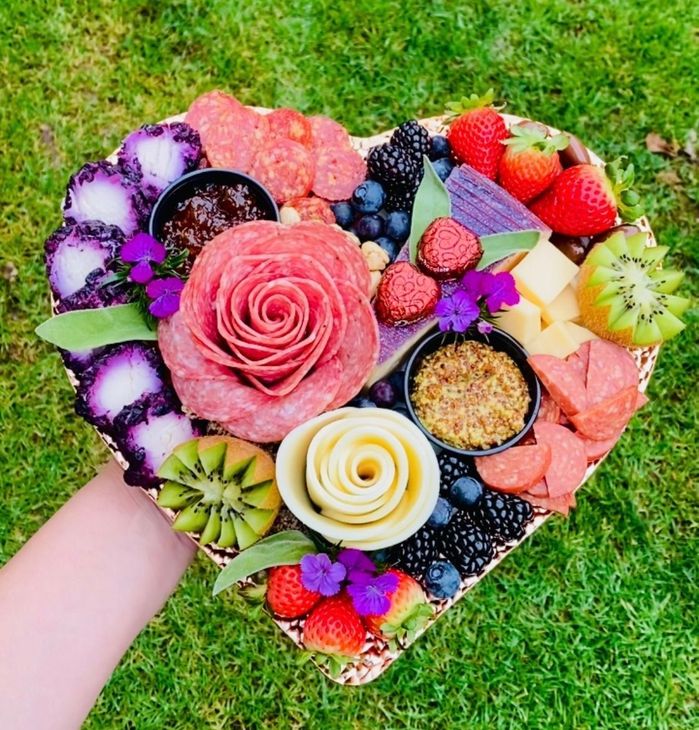 Charcuterie board with cheese, crackers, fruit, and flowers.