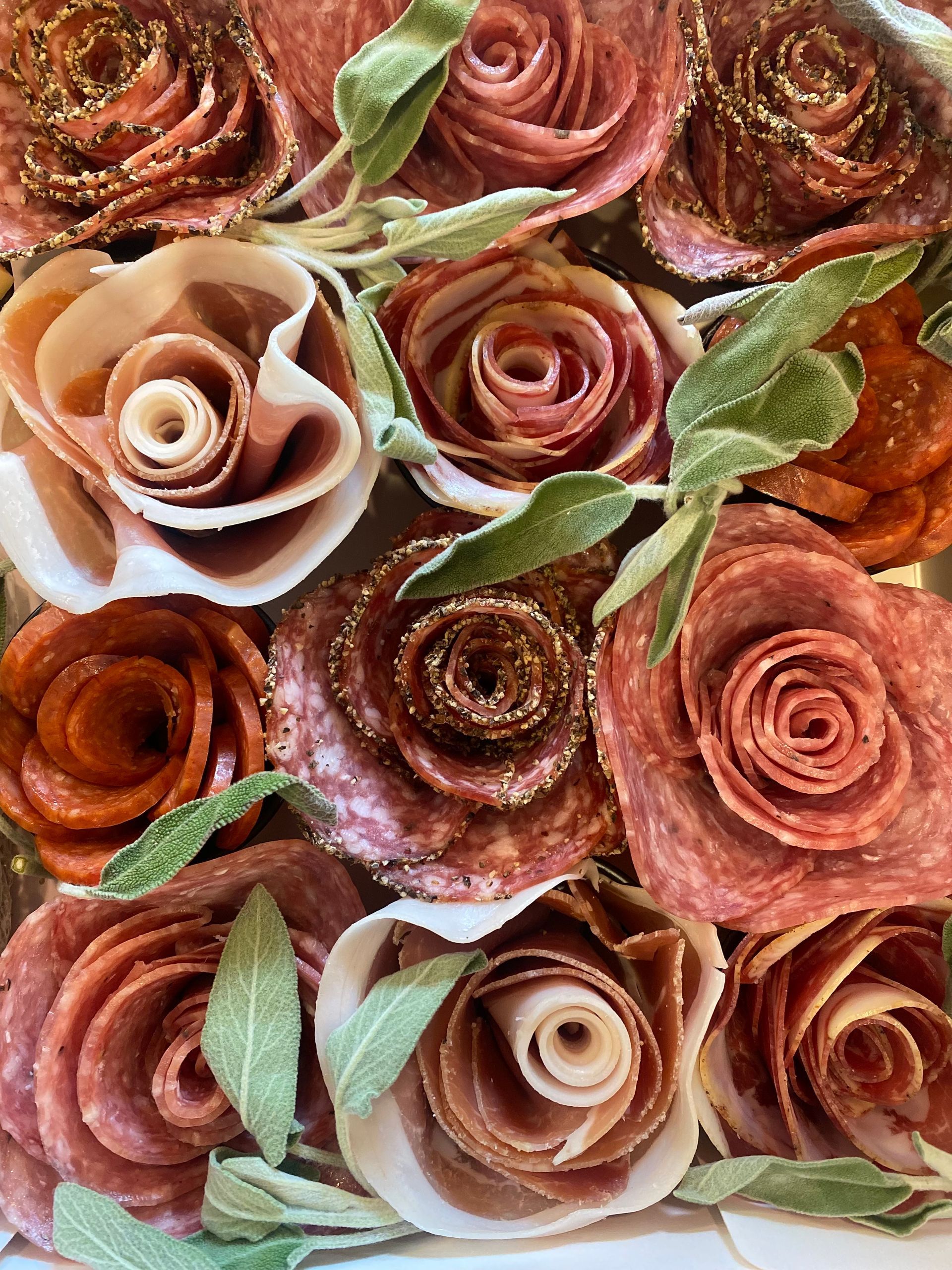 Salami roses arranged with green leaves; a charcuterie presentation.