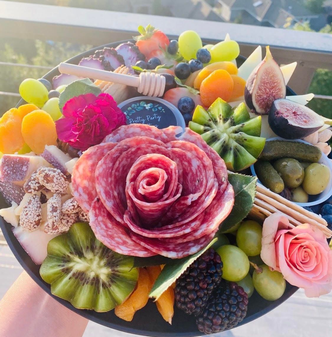 Charcuterie board with salami rose, fruit, cheese, and olives.