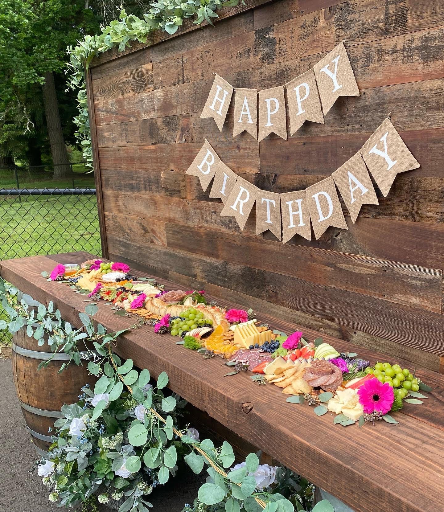 Rustic wooden display with birthday banner and food spread decorated with flowers.