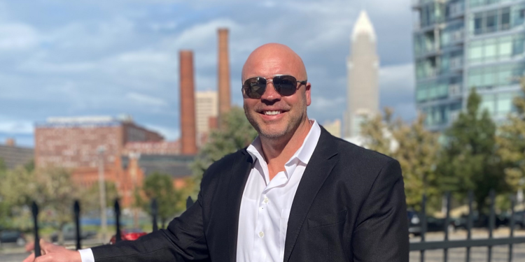 A man in a suit and sunglasses is standing in front of a city.